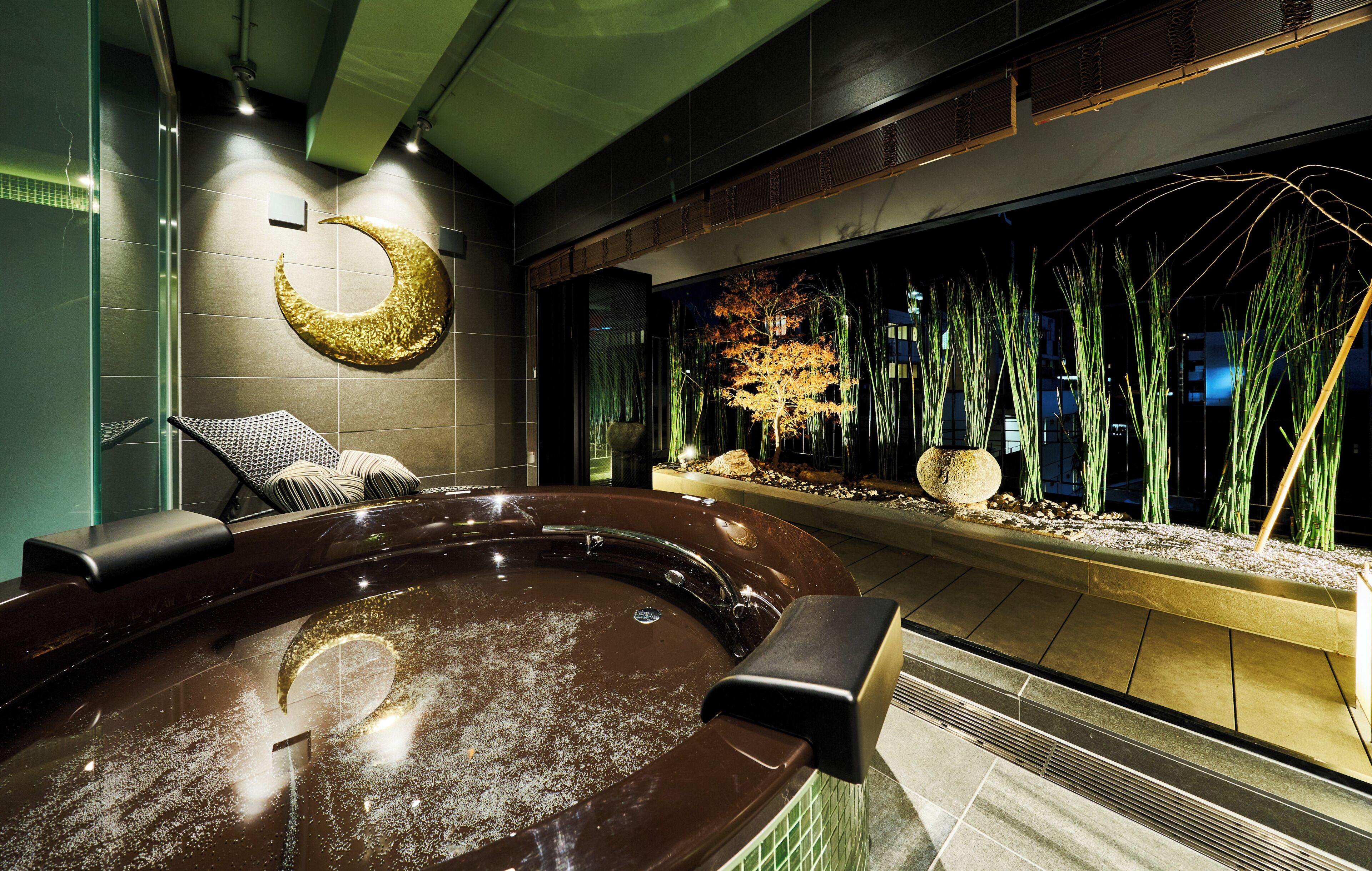 Un jacuzzi con decoración de luna creciente, una pared de vidrio con plantas de interior y una zona de estar.