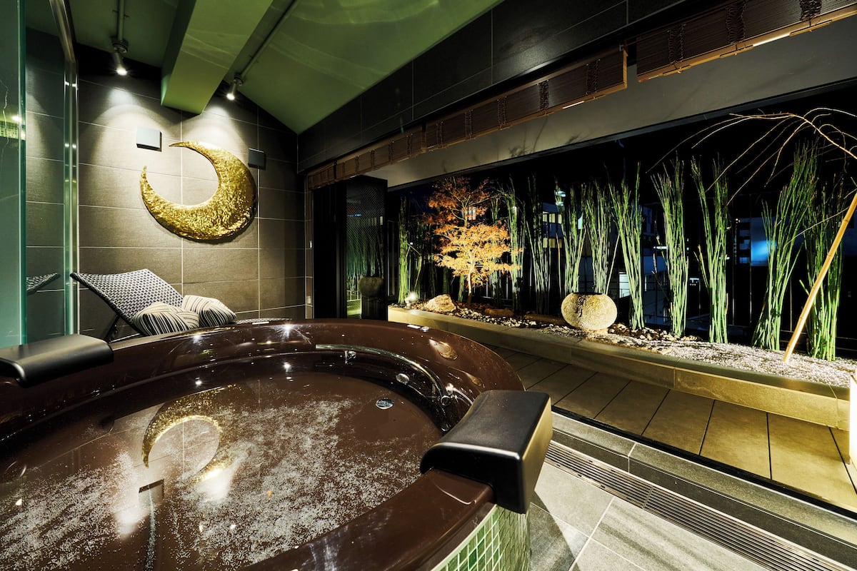 Un jacuzzi con decoración de luna creciente, una pared de vidrio con plantas de interior y una zona de estar.