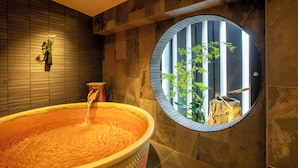 Een wellnessruimte met een ruim bubbelbad, een houten wand en een rond raam met uitzicht op planten.