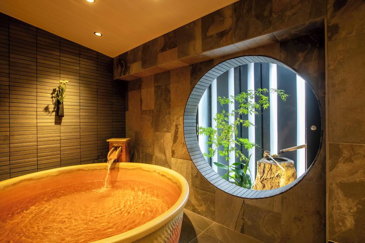 Un'area benessere con una vasca idromassaggio ampia, una parete in legno e una finestra circolare che si affaccia su piante.