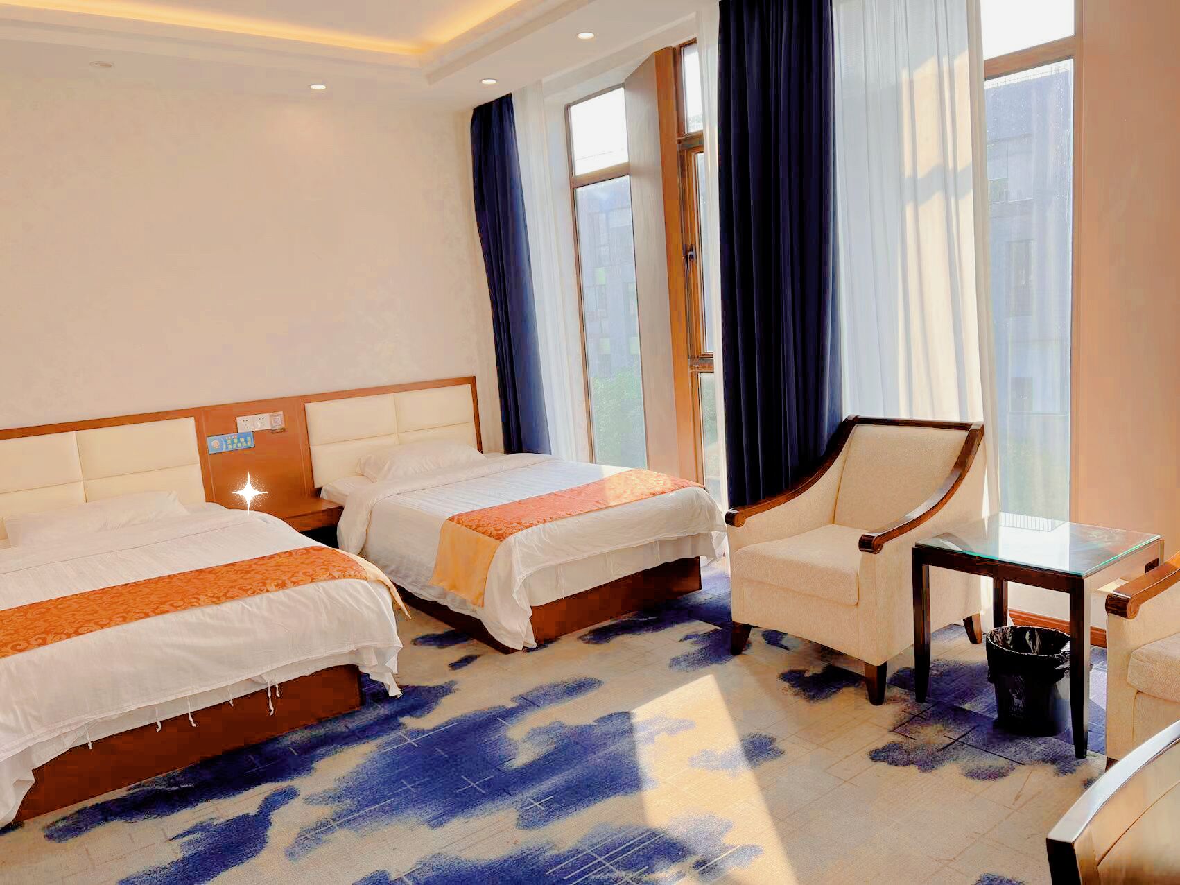 Ein Hotelzimmer mit zwei Betten, einem Sessel, einem kleinen Tisch und einem Fenster mit Vorhängen.