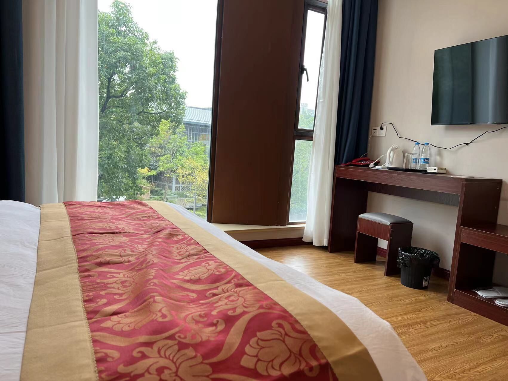 Hotelkamer met een groot bed, een bureau met een computer, een televisie en uitzicht op bomen.