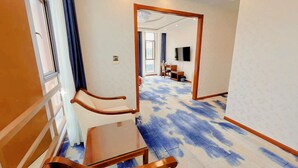 Ein Hotelzimmer mit einem großen Spiegel, einem Holzstuhl, einem kleinen Tisch und einem blau gemusterten Teppich.