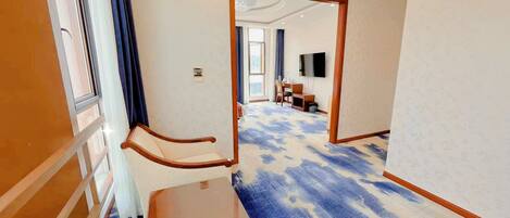 Quarto de hotel com um espelho grande, uma cadeira de madeira, uma mesa pequena e um tapete azul estampado.