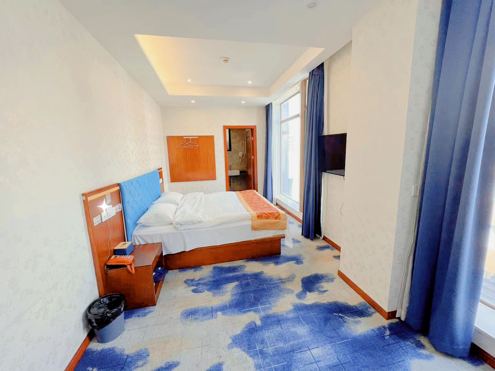 Habitación de hotel con cama, escritorio, silla, televisor y ventana con cortinas.