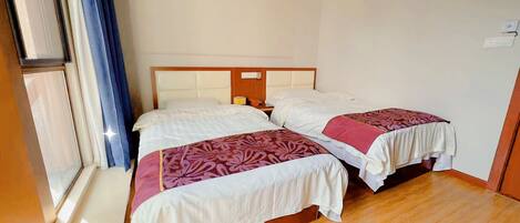 A hotel room with two beds, wooden flooring, a window with curtains, and a white wall.