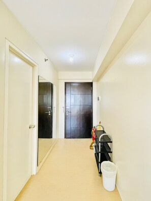 A hallway with a light-colored floor, a black door at the end, and a cleaning cart with a white bucket. - Hubomoto Avida Suites (Iloilo)