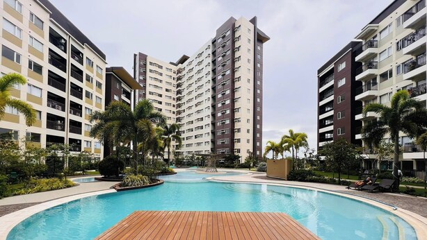 A swimming pool with a wooden deck in the foreground, surrounded by multi-story residential buildings with balconies.