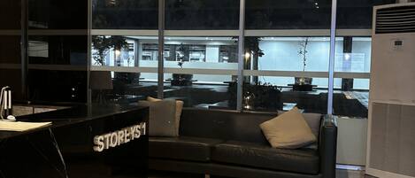 A modern interior with a reception desk labeled "STOREYS," a black leather sofa, and large windows offering a view of the outside.