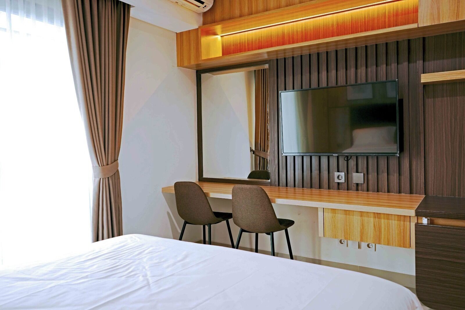A hotel room with a bed, a desk with two chairs, a large mirror, and a television.