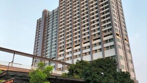 Un edificio de gran altura con varios pisos, una entrada vigilada y un corredor cubierto.