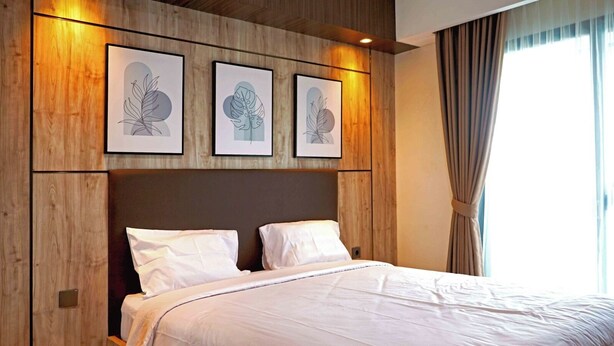 Una habitación de hotel con cabecera de madera, una cama grande con ropa blanca y tres láminas botánicas enmarcadas en la pared.