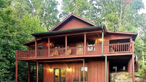 Une cabane en bois à deux étages, dotée d’un balcon, d’une véranda et d’une allée gravillonnée.