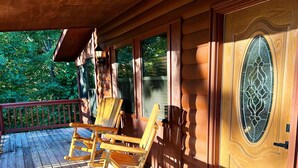 Une terrasse en bois avec des fauteuils à bascule et une porte ornée d’un panneau de verre décoratif.