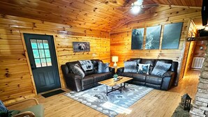 L’intérieur d’un chalet confortable, avec un plancher en bois, deux canapés en cuir, une table basse et une cheminée en pierre.