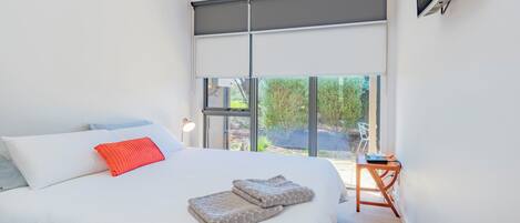 A bedroom with a large bed, a red pillow, and a view of greenery outside.