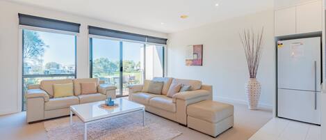 Una sala de estar moderna con un sofá beige, una mesa de centro blanca y un ventanal con vistas al exterior.