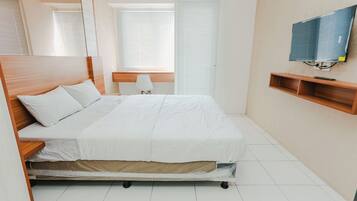 A bedroom with a bed, a desk, a chair, a TV, and a window with blinds.