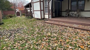 Ein Haus mit überdachter Terrasse, einem Steinkamin und einem umzäunten Garten mit herabgefallenen Blättern.