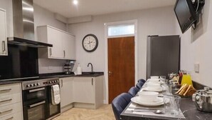 Une cuisine moderne avec des meubles blancs, une cuisinière noire et un coin repas avec une table dressée pour quatre personnes.