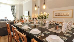 Un coin repas avec une longue table dressée pour le repas, des chaises et un vase rempli de fleurs.