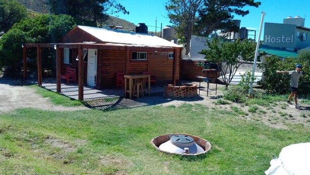 Una cabaña rústica de madera con un porche cubierto, zona de barbacoa y un pozo de fuego.