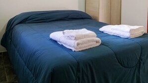 Una cama con una colcha azul y dos toallas blancas dobladas con cuidado a un lado.