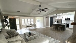 A spacious living room with a sofa, ottoman, and coffee table, a dining area with chairs, a kitchen with modern appliances, and a ceiling fan. - Newly remodeled 3 BR house, 5 min from WEC and by golf course. Dogs allowed (Ocala)