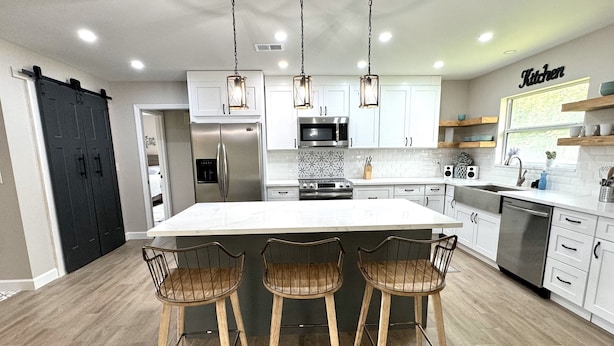 A modern kitchen with white cabinetry, a large island, and three bar stools. - Newly remodeled 3 BR house, 5 min from WEC and by golf course. Dogs allowed (Ocala)