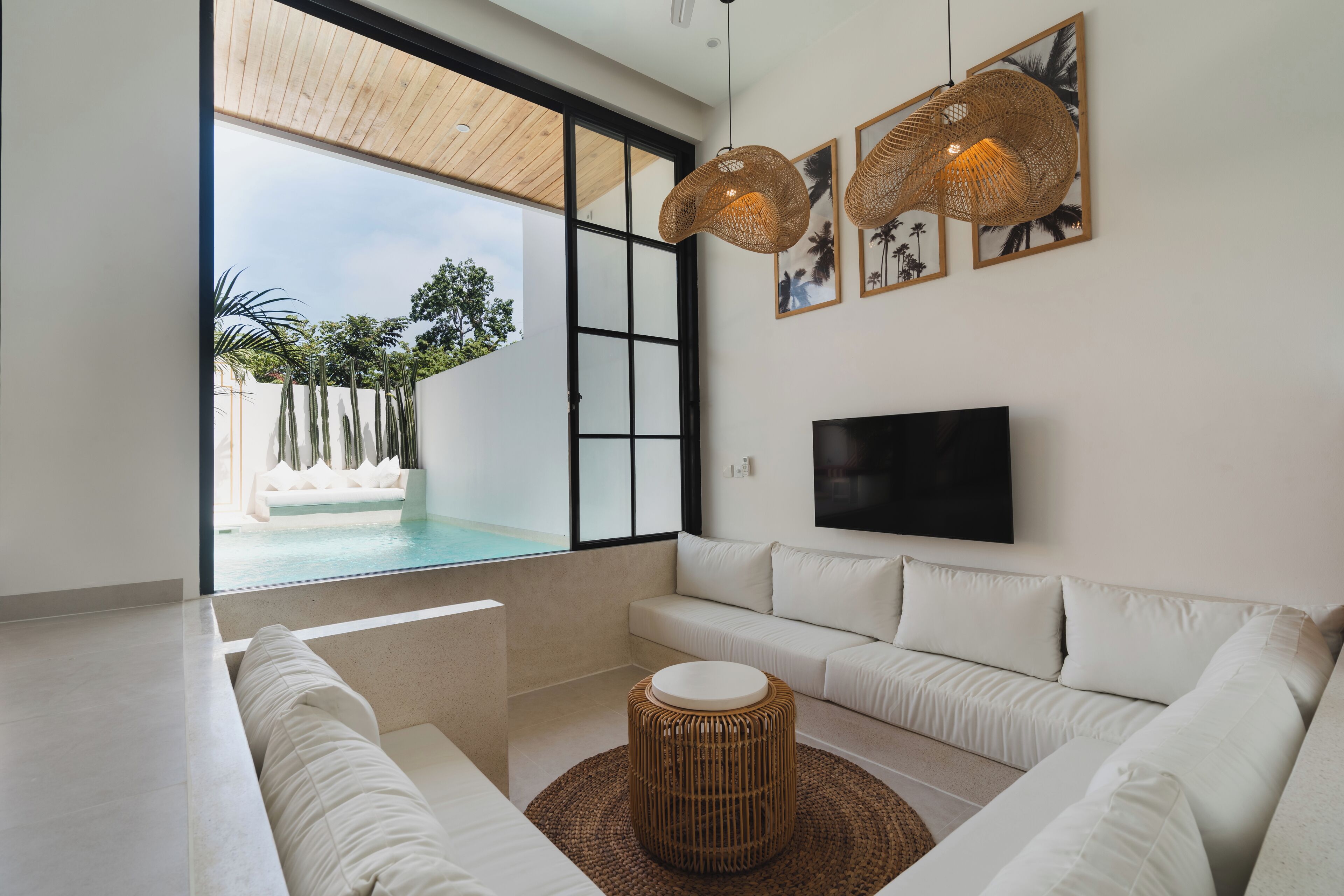 Een moderne woonkamer met een groot raam, een witte bank, een televisie en een rieten salontafel.