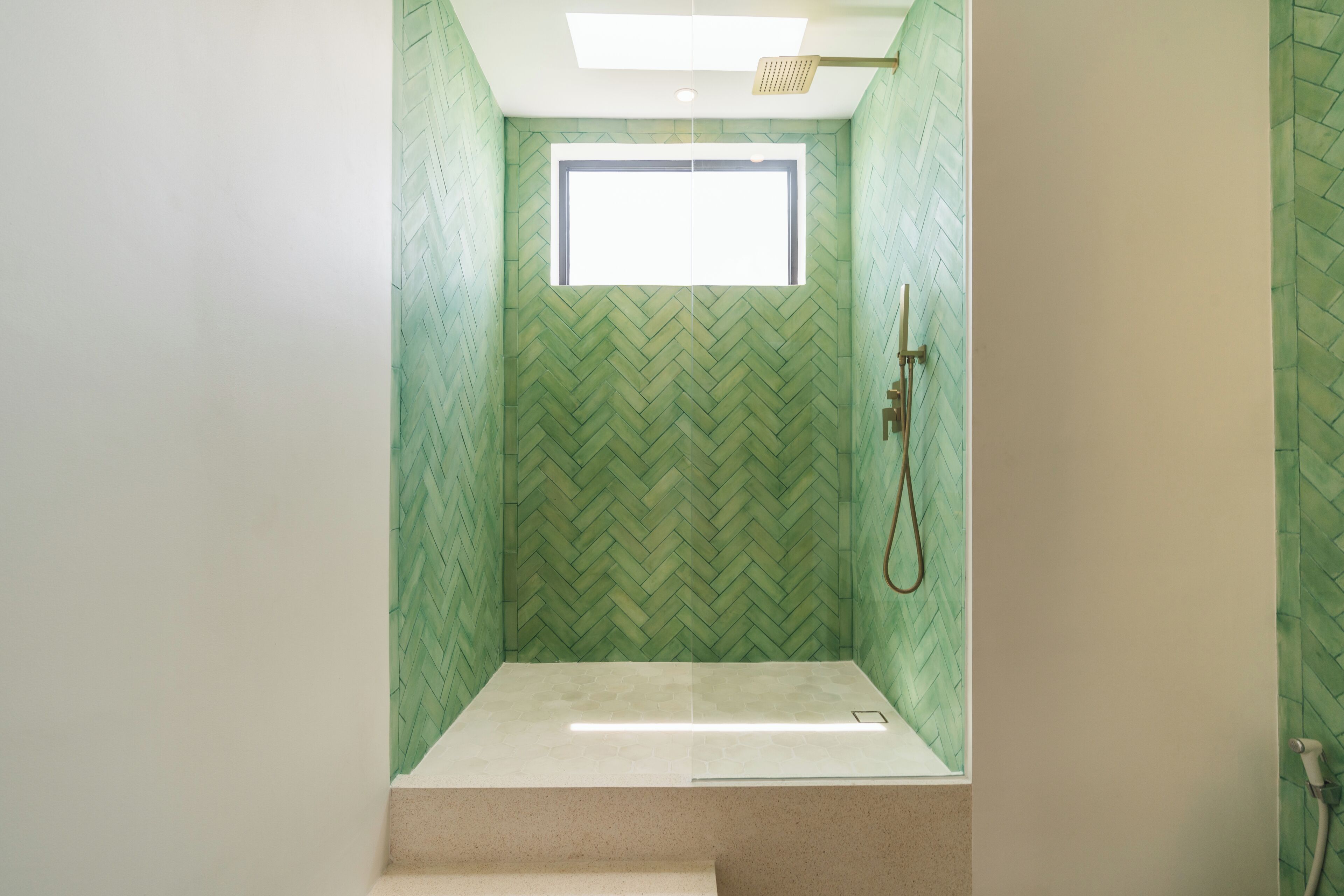 Une douche avec un mur orné d’un motif en chevrons, une petite fenêtre et un pommeau de douche.