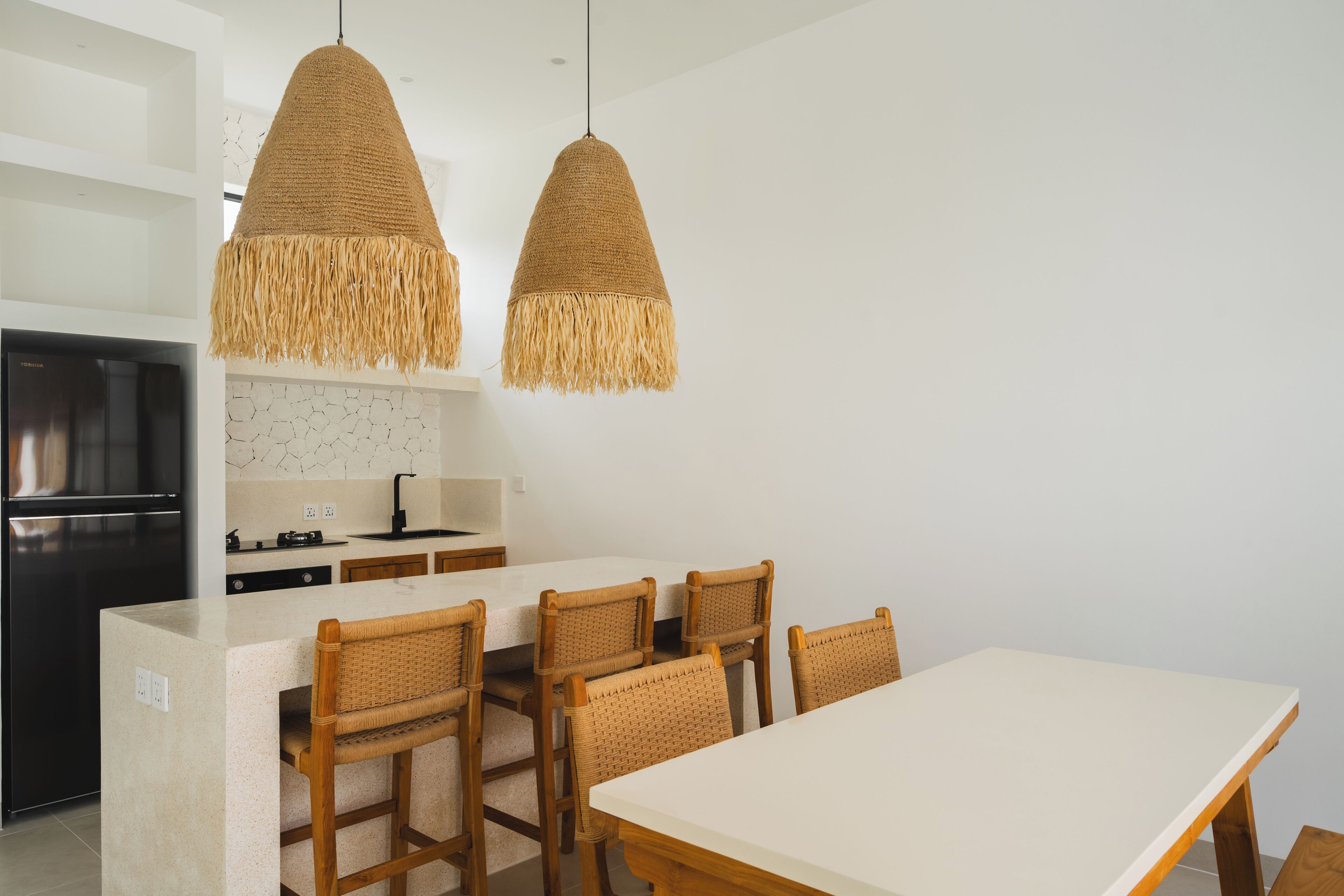 A modern kitchen with a central island, wooden chairs, and two hanging pendant lights.
