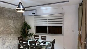 Un comedor con una mesa de vidrio, cuatro sillas, una planta en maceta y una lámpara en el techo.