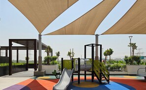 Kids can play under the shade of the outdoor play area's sail canopies, surrounded by climbing frames and a slide.