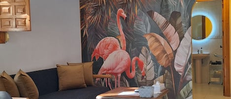 Una sala de estar moderna con un sofá, una mesa de centro y un mural en la pared con flamencos y hojas tropicales.