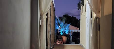 A corridor with a tiled floor leading to an outdoor area with a potted plant and a decorative light.