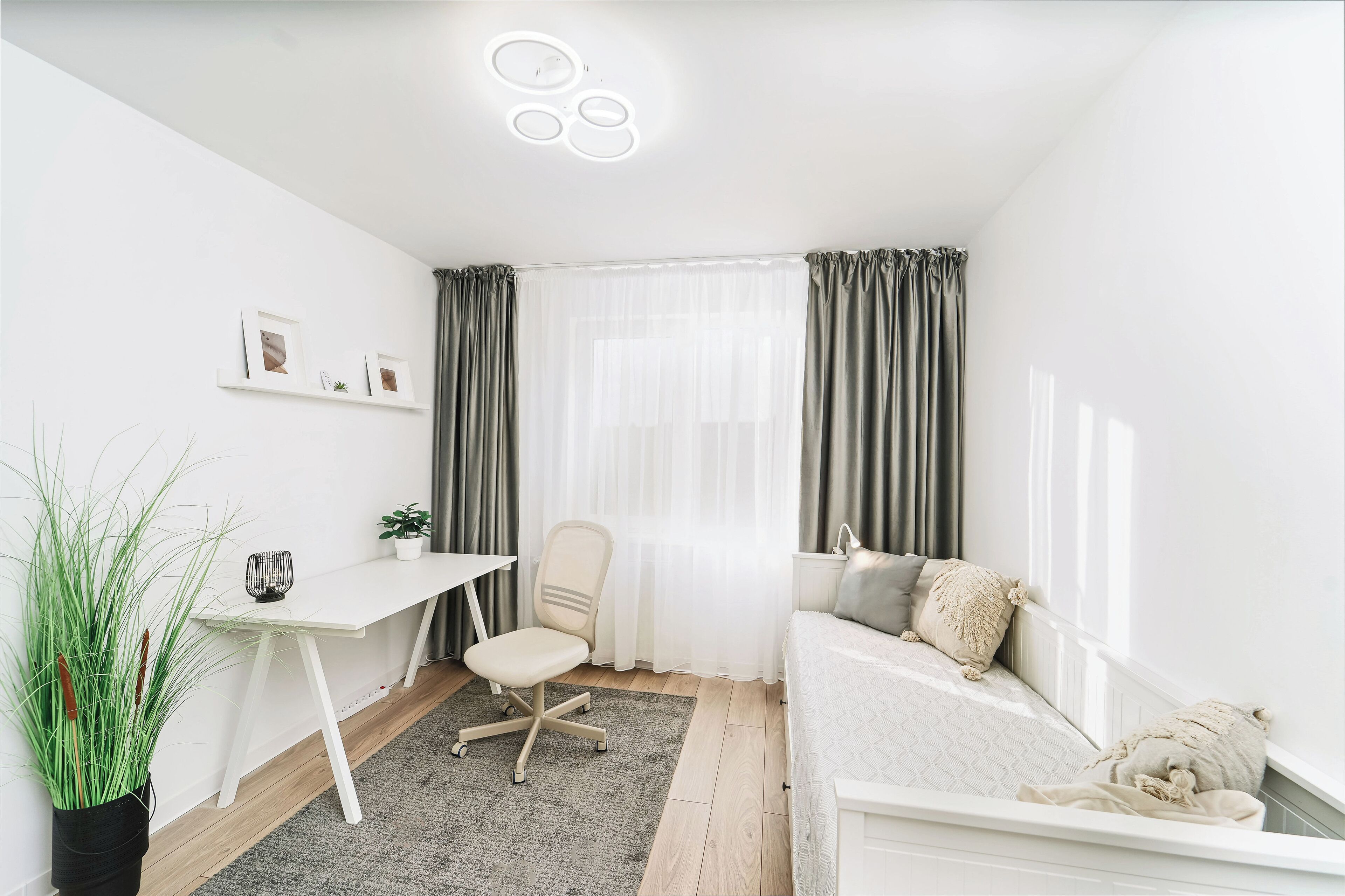 A modern, minimalist bedroom with a white desk, a comfortable sofa, and a large window with curtains.