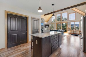 A modern kitchen with dark cabinetry, a large island, and a view of the outdoors through large windows.