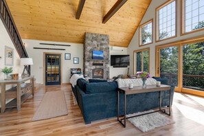 A spacious living room with a stone fireplace, a large window, and a wooden ceiling. - Outlook at The Peaks (Newry)