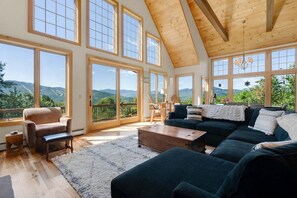 A spacious living room with large windows, a wooden ceiling, and a view of mountains.