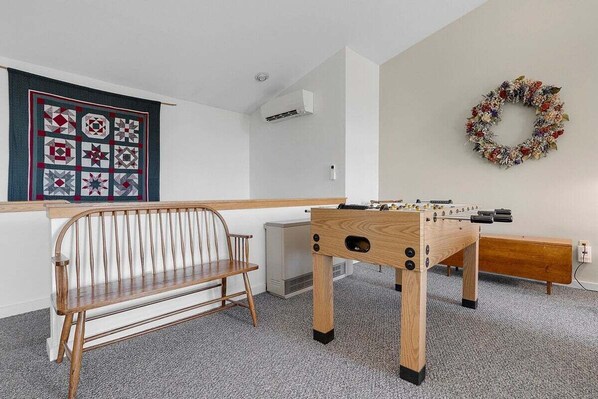 A room with a wooden bench, a foosball table, a wall-mounted air conditioner, and a decorative wreath.