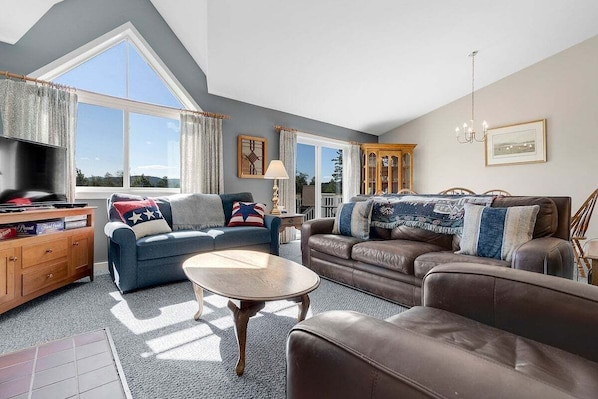 A spacious living room with a large window, a television, a wooden cabinet, and two sofas.