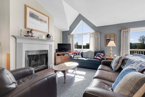 A living room with a fireplace, a television, a sofa, and a large window.