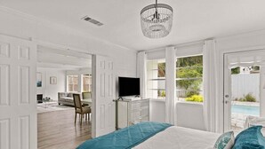A bedroom with a bed, a TV, a desk, and a view of a swimming pool. - Driftwood Cottage | Luxury 3BR Pool Home Steps to East Beach St. Simons Island (Saint Simons Island)