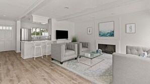 A modern living room with a fireplace, a flat-screen TV, and a dining area with bar stools. - Driftwood Cottage | Luxury 3BR Pool Home Steps to East Beach St. Simons Island (Saint Simons Island)