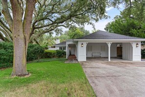 A house with a covered porch, a driveway, and a large tree in the foreground.