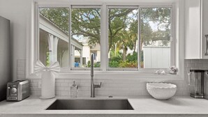 A kitchen with a large window, a Bosch dishwasher, a white sink, and a toaster. - Driftwood Cottage | Luxury 3BR Pool Home Steps to East Beach St. Simons Island (Saint Simons Island)