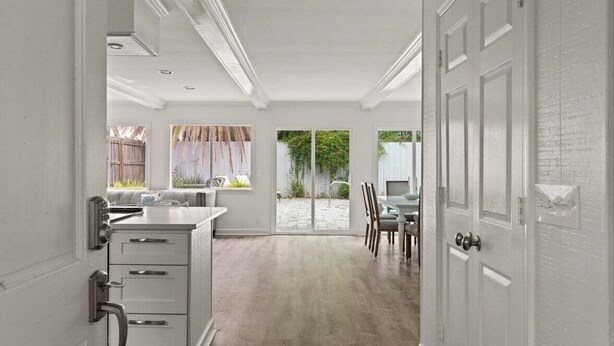 A spacious kitchen with a large island, a dining area with chairs, and a view of the backyard through large windows. - Driftwood Cottage | Luxury 3BR Pool Home Steps to East Beach St. Simons Island (Saint Simons Island)