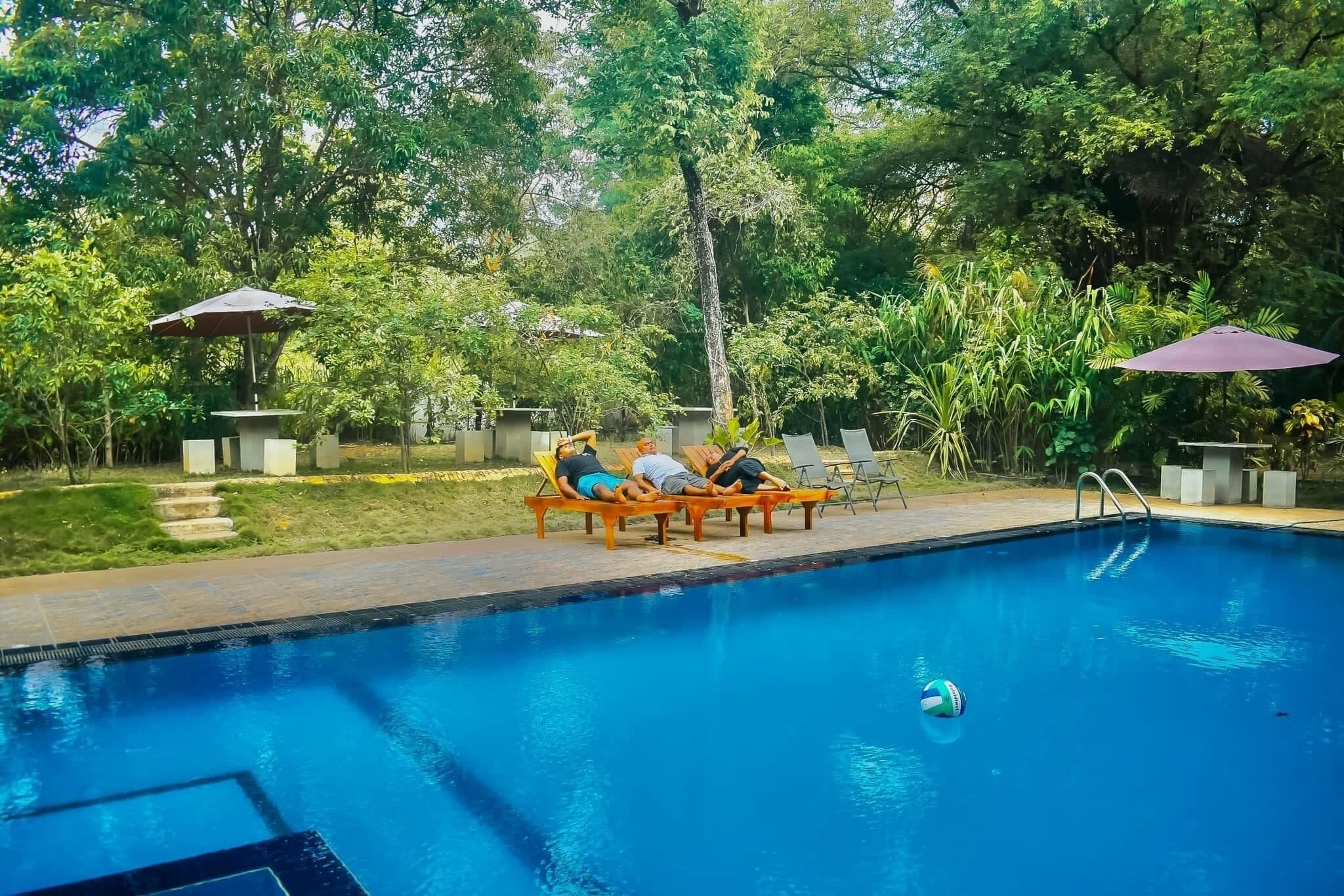 Un espace piscine agrémenté de chaises longues et de parasols, le tout entouré d’une végétation luxuriante.