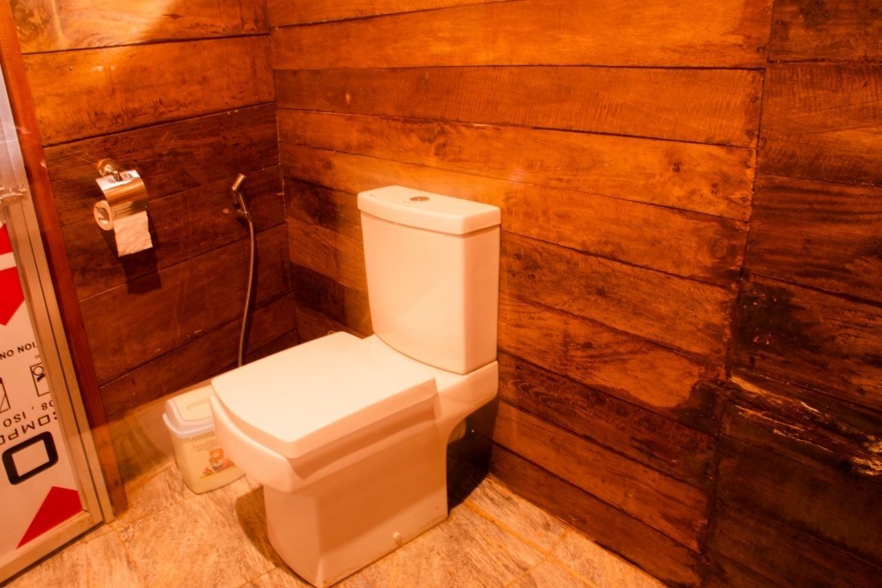 A small, wooden-paneled bathroom with a white toilet, a shower hose, and a toilet paper holder.